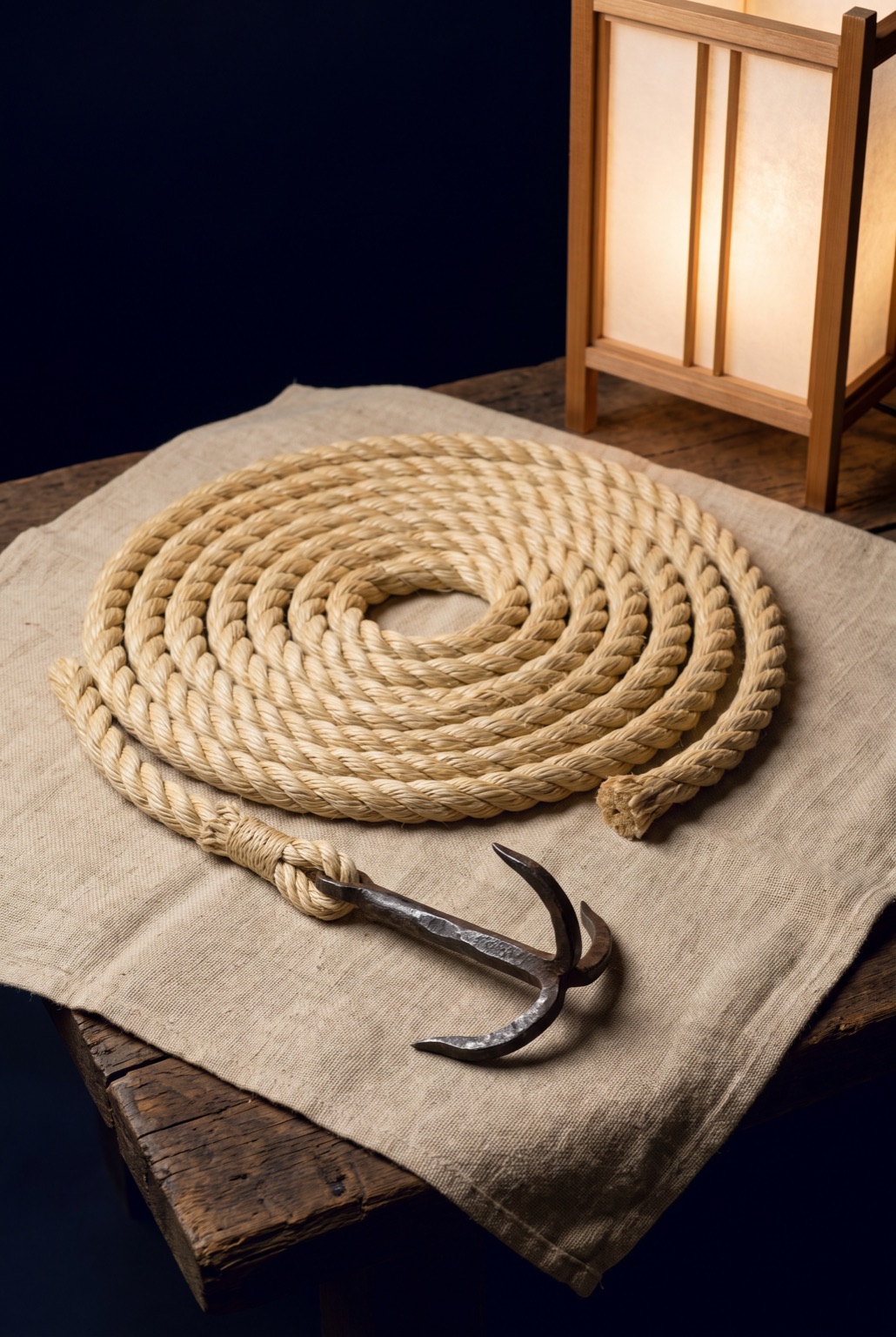 A coil of pale hand-laid hemp rope with a four-pronged forged iron grapple spliced to its end.